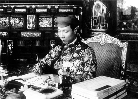 Vua Khải Định trong trang phục thường triều, đầu đội khăn xếp, đang làm việc trong điện Cần Chánh