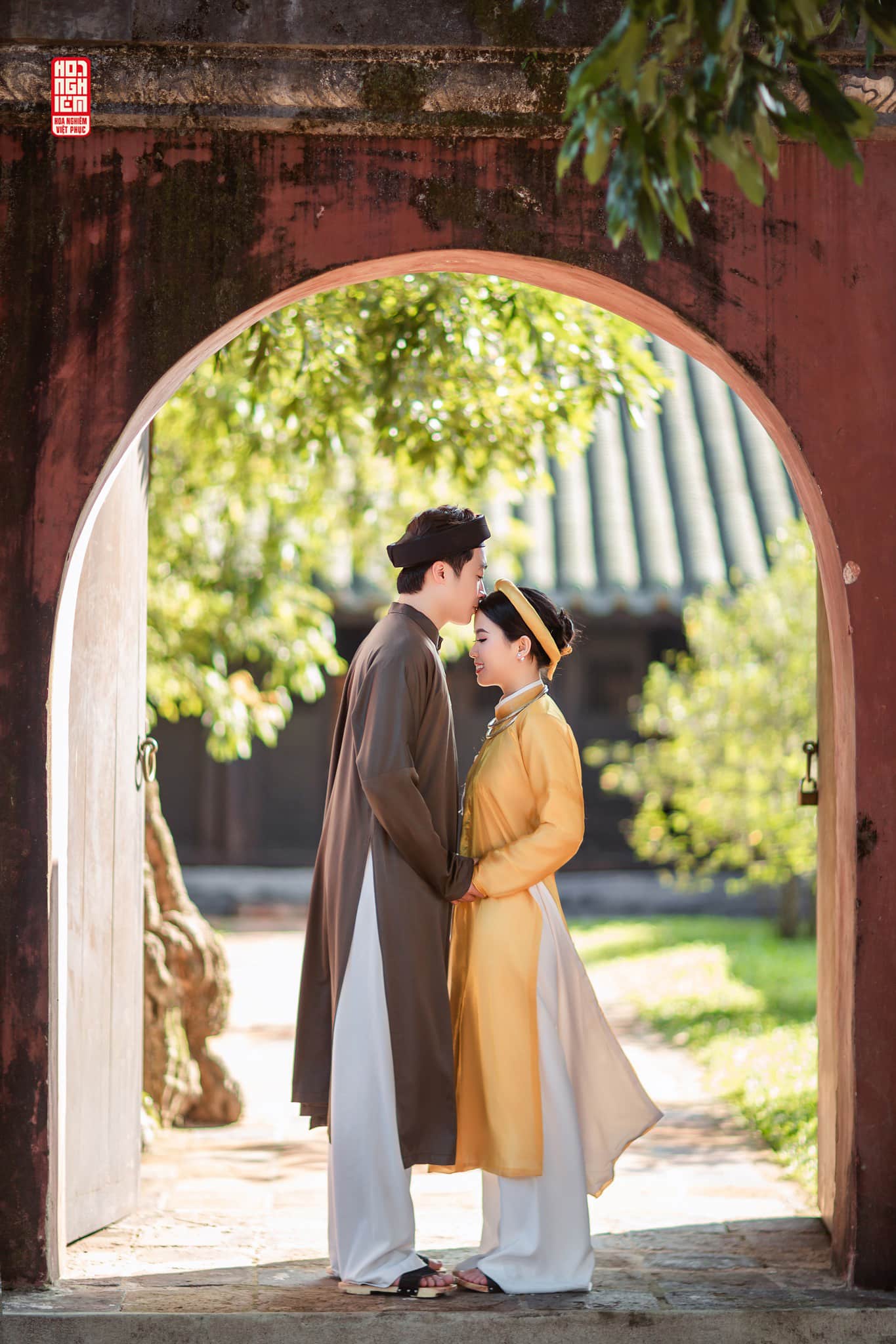 Cổ phục cưới – Ngũ Thân Cát Duyên | Khoảnh khắc giao hòa Cặp đôi trong cổ phục cưới Ngũ Thân Cát Duyên đứng dưới vòm cổng cổ, tay trong tay, không gian cung đình xưa.
