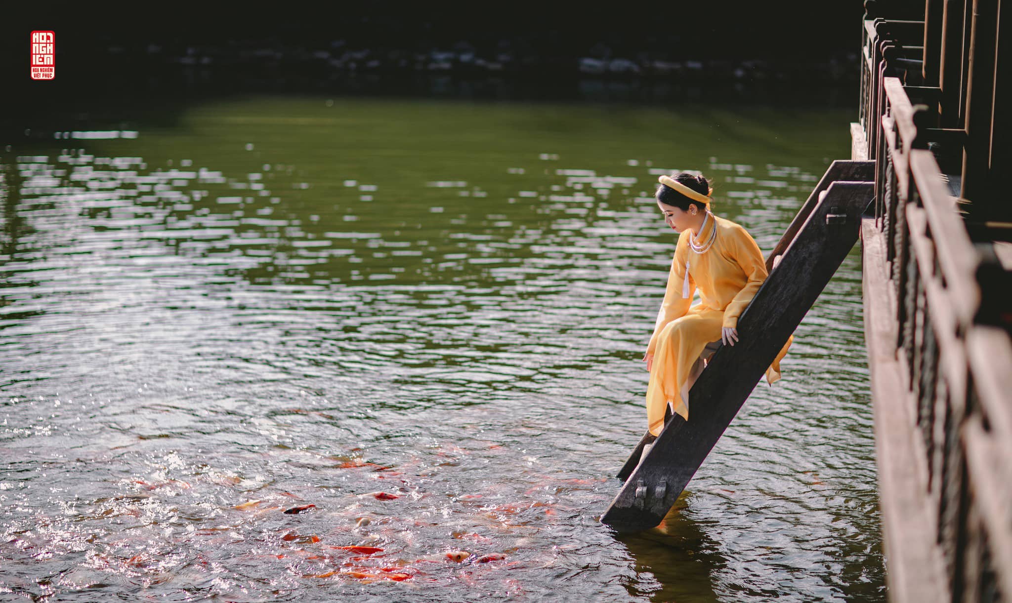 Nữ phục Ngũ Thân Cát Duyên bên thủy tạ Nữ phục Ngũ Thân màu hoàng thổ trong cổ phục cưới Cát Duyên bên bậc gỗ thủy tạ, không gian yên bình