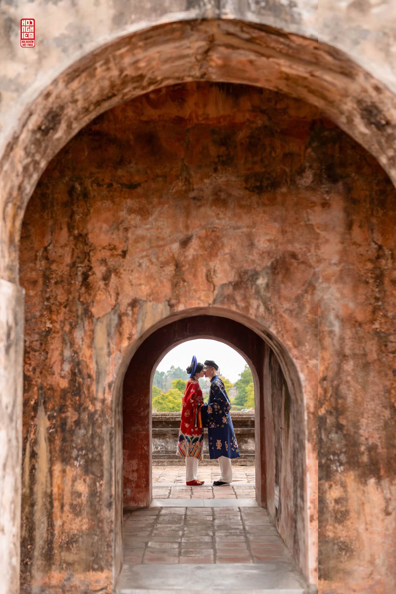 Việt phục cưới Nhật Bình – Áo Tấc Phúc Duyên Hòa Hợp qua cổng vòm cổ Cặp đôi trong Việt phục cưới Nhật Bình – Áo Tấc Phúc Duyên Hòa Hợp đứng đối diện nhau qua cổng vòm Hoàng thành Huế