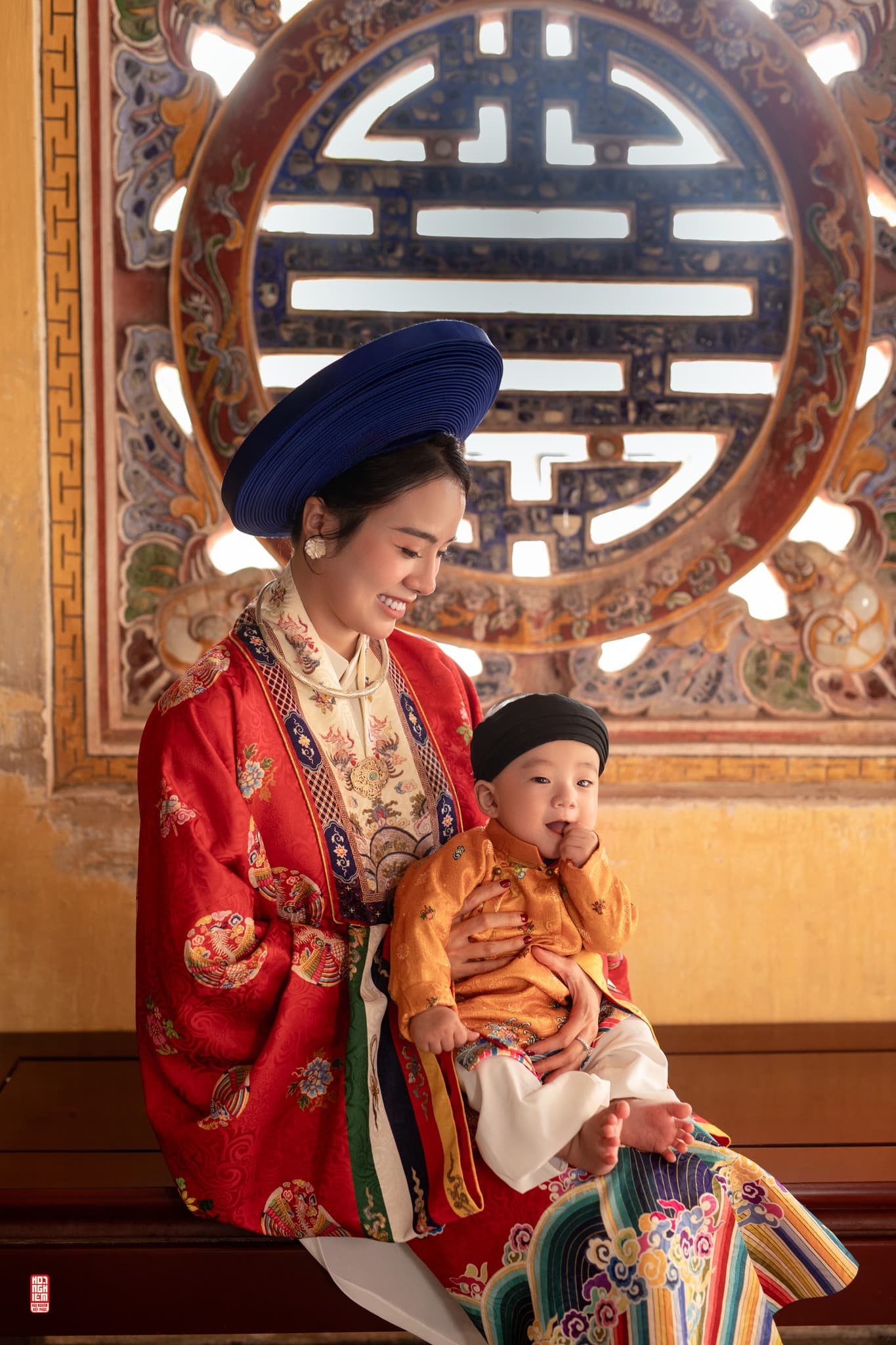Mẹ mặc áo Nhật Bình đỏ bế em bé mặc Ngũ Thân tay chẽn trong không gian cung đình Huế