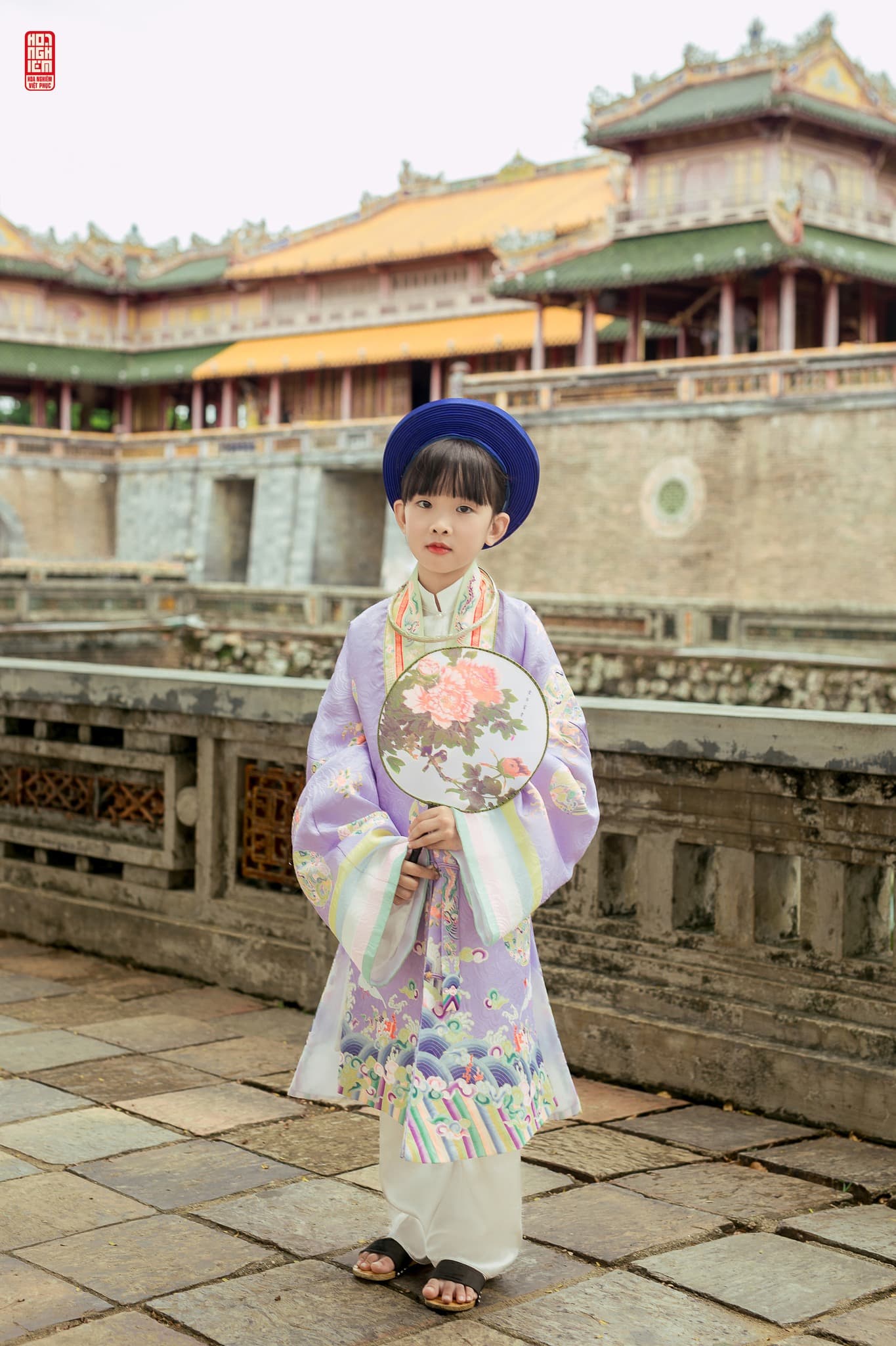 Cổ phục Nhật Bình tím cho bé gái phong cách cung đình Bé gái mặc áo Nhật Bình tím truyền thống cầm quạt tròn trước Đại Nội Huế