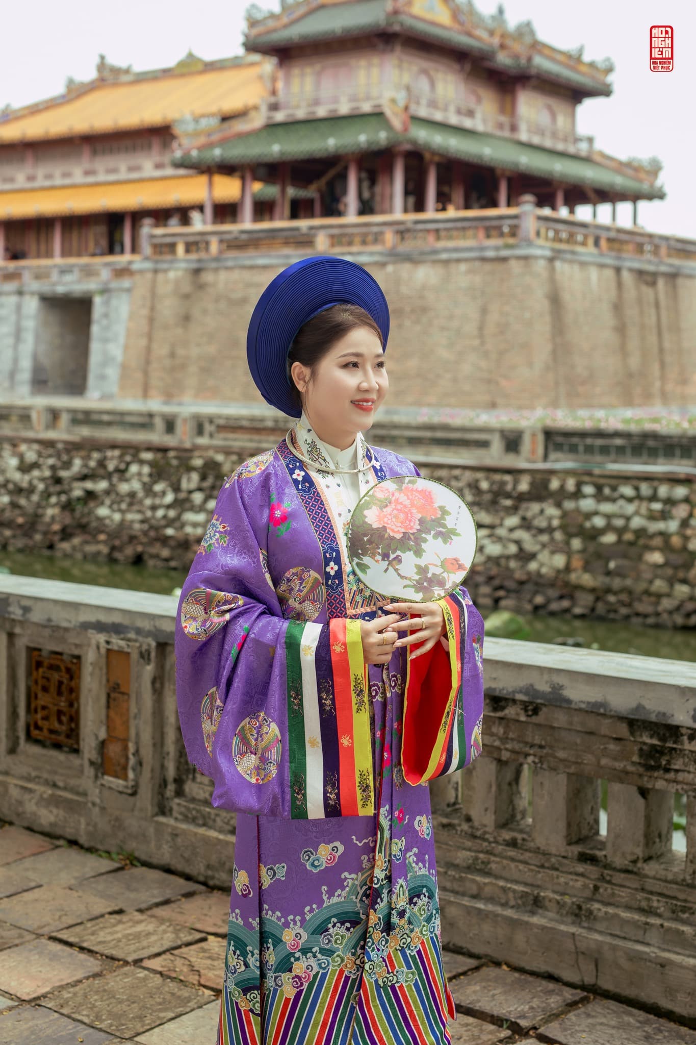 Áo Nhật Bình tím nữ phong cách cung đình Huế cao cấp Phụ nữ mặc áo Nhật Bình tím truyền thống cầm quạt tròn chụp tại cung đình Huế
